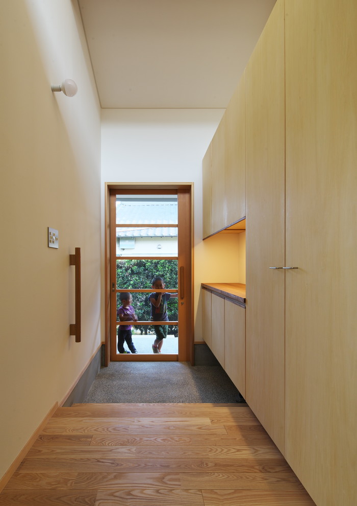 Cette image montre une entrée minimaliste de taille moyenne avec un couloir, un mur beige, un sol en bois brun, une porte coulissante, une porte en bois brun et un sol beige.