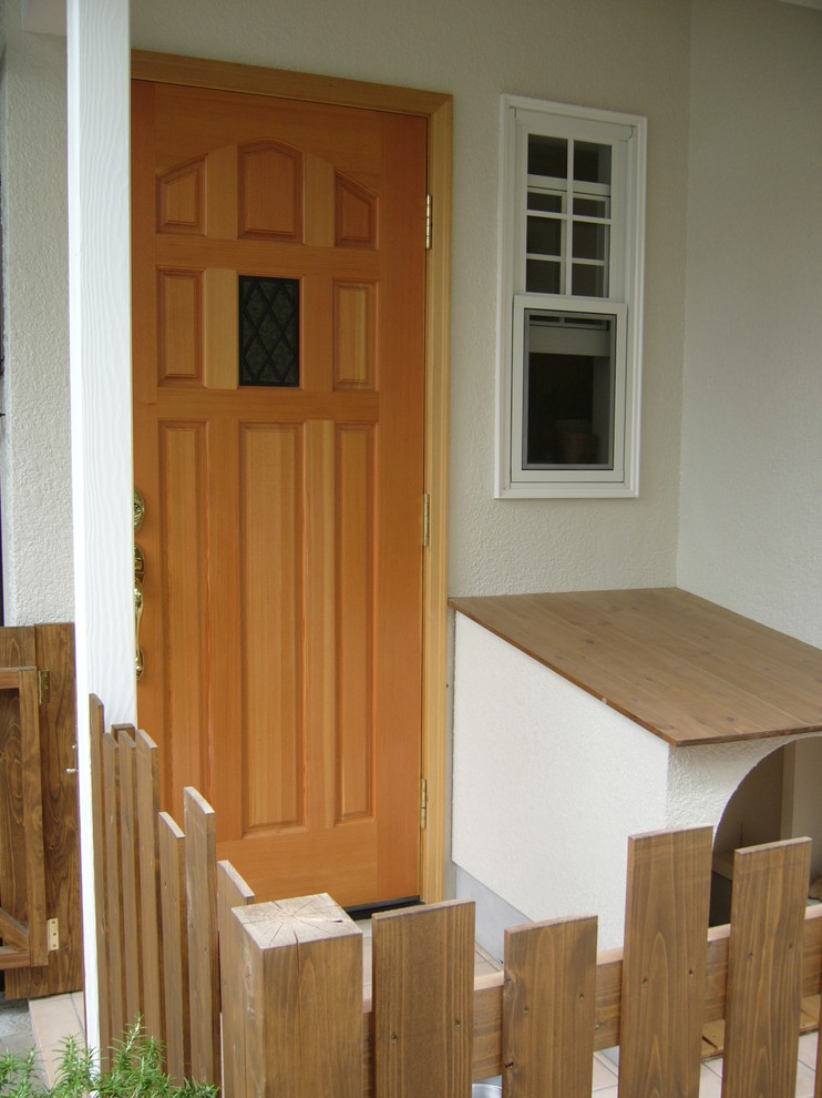 Aménagement d'une petite porte d'entrée classique avec un mur blanc, tomettes au sol, une porte simple, une porte en bois clair et un sol rose.