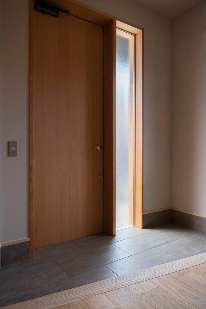 横浜にある小さなモダンスタイルのおしゃれな玄関ドア (ベージュの壁、磁器タイルの床、木目調のドア、グレーの床) の写真