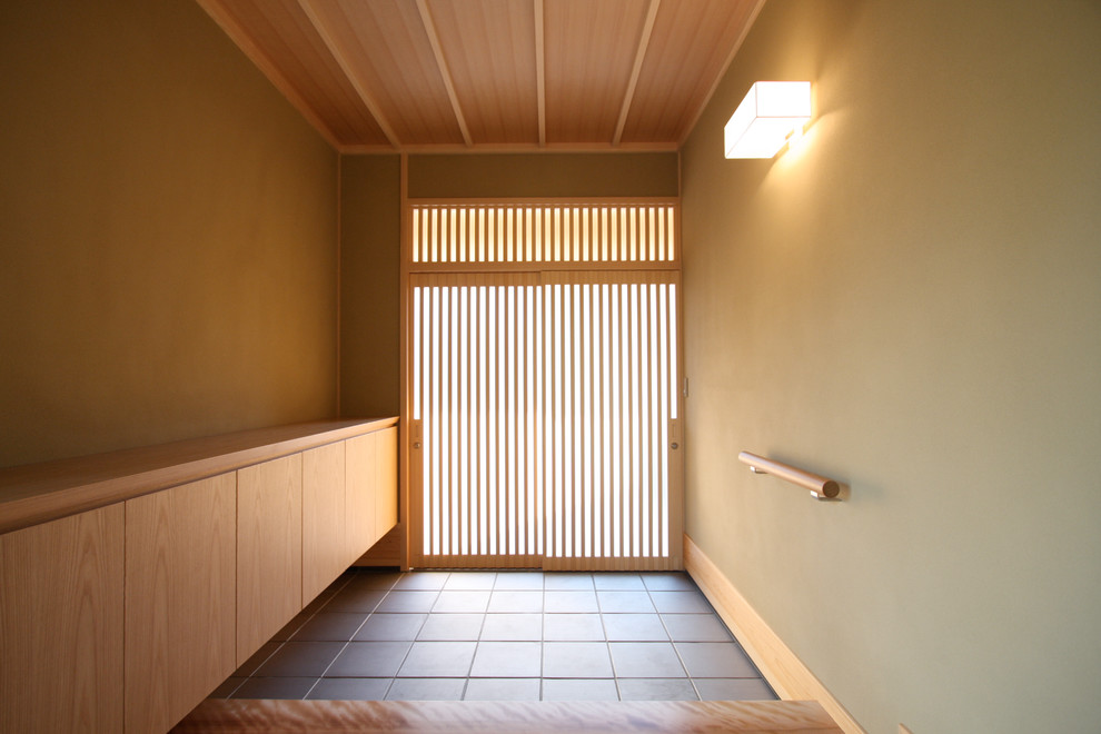 На фото: маленькая узкая прихожая в восточном стиле с бежевыми стенами, полом из керамической плитки, раздвижной входной дверью, входной дверью из светлого дерева и серым полом для на участке и в саду