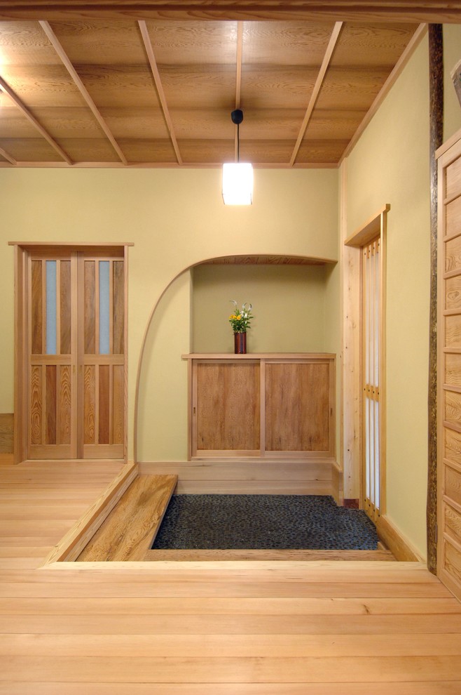 Diseño de entrada asiática con paredes beige, suelo de madera clara, puerta corredera y suelo marrón