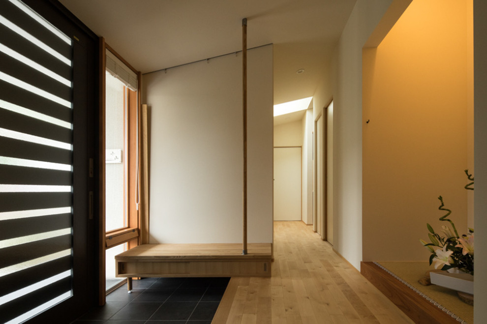На фото: узкая прихожая среднего размера в восточном стиле с белыми стенами, полом из керамогранита, раздвижной входной дверью, черной входной дверью и серым полом