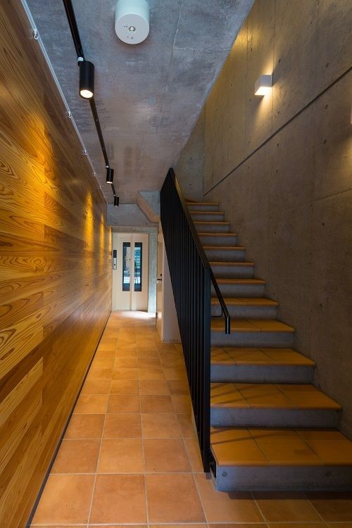 Cette image montre une grande entrée minimaliste avec un couloir, un mur marron, tomettes au sol, une porte simple, une porte en verre et un sol marron.