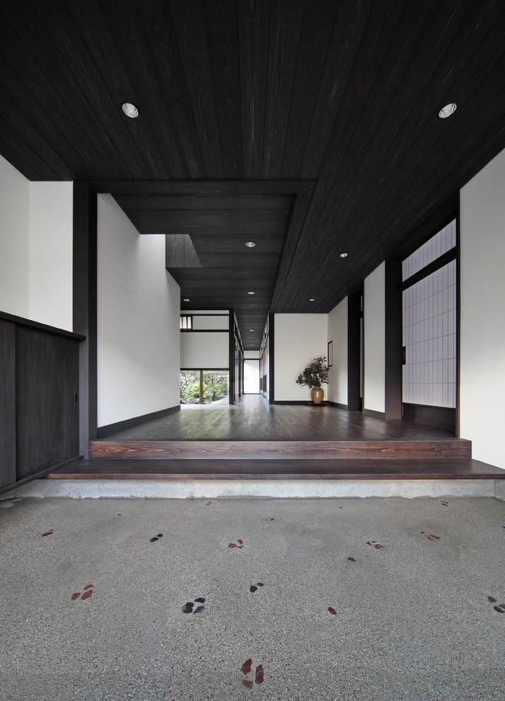 Bild på en mellanstor orientalisk hall, med vita väggar, betonggolv, en skjutdörr, en svart dörr och grått golv