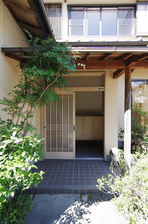 Aménagement d'une porte d'entrée asiatique avec un mur blanc, sol en granite, une porte coulissante et une porte en bois clair.