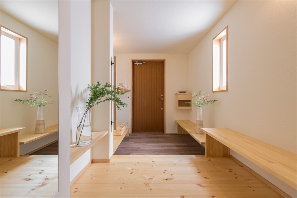 Aménagement d'une entrée scandinave avec un mur blanc, une porte simple, une porte en bois brun et un sol marron.
