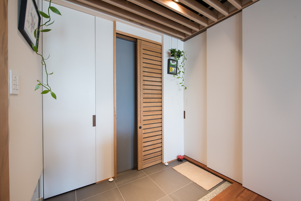 Идея дизайна: маленькое фойе в современном стиле с белыми стенами, полом из керамогранита, раздвижной входной дверью, входной дверью из светлого дерева и серым полом для на участке и в саду