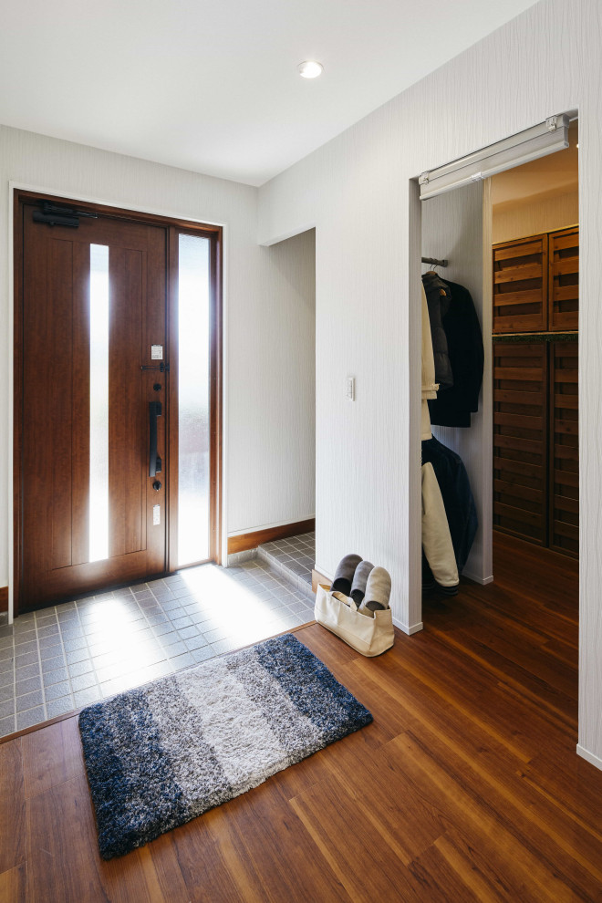 Cette photo montre une entrée de taille moyenne avec un vestiaire, un mur blanc, un sol en bois brun, une porte simple, une porte en bois foncé et un sol marron.