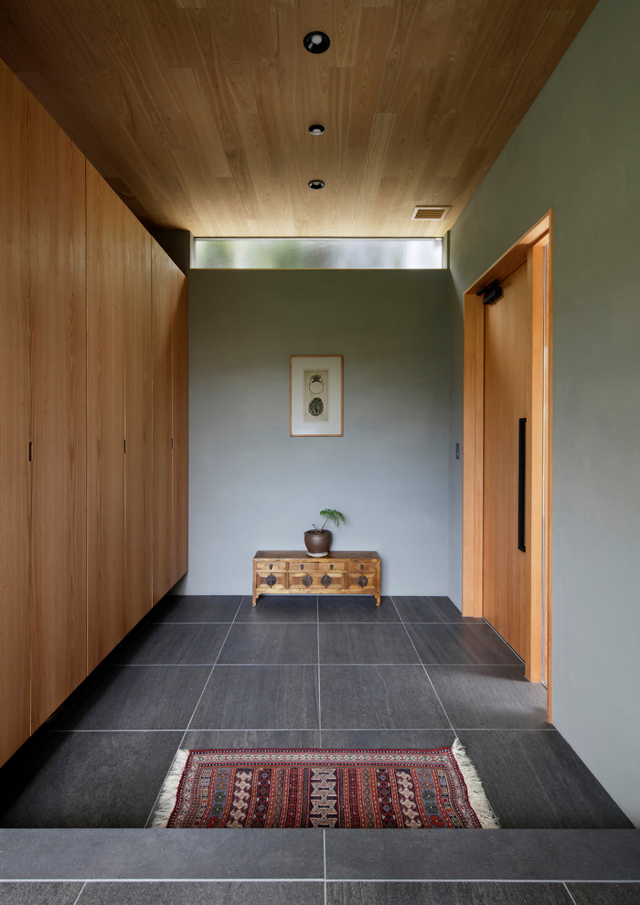 На фото: узкая прихожая в восточном стиле с серыми стенами, одностворчатой входной дверью, входной дверью из дерева среднего тона и серым полом с