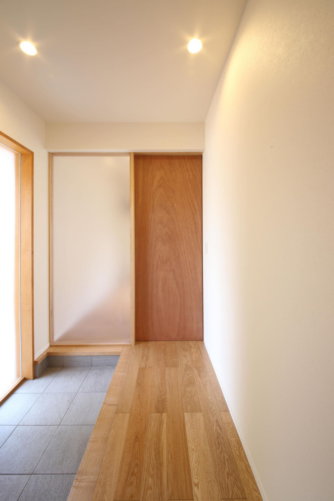 This is an example of a medium sized modern hallway with white walls, a single front door, a medium wood front door, grey floors, porcelain flooring, a wallpapered ceiling and wallpapered walls.