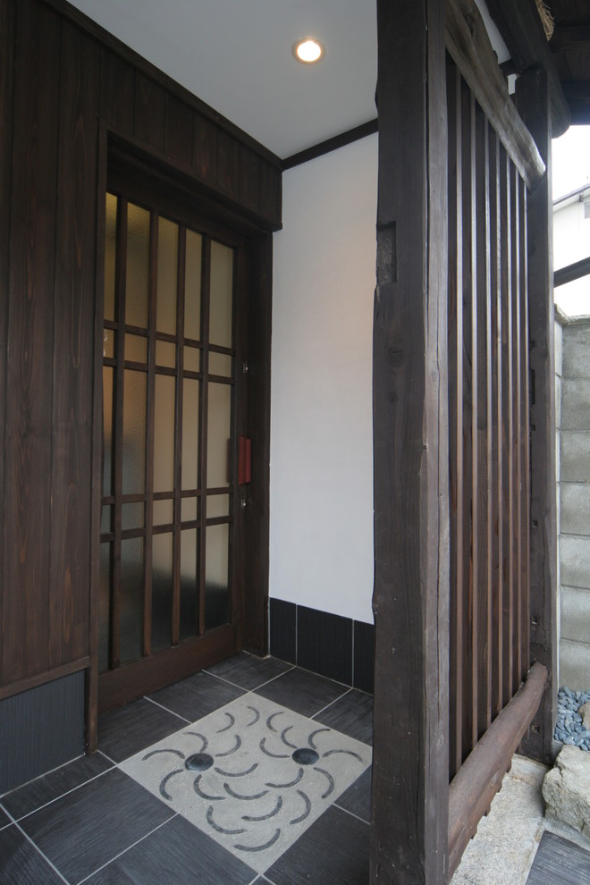 他の地域にある小さな和風のおしゃれな玄関 (白い壁、磁器タイルの床、濃色木目調のドア、黒い床) の写真
