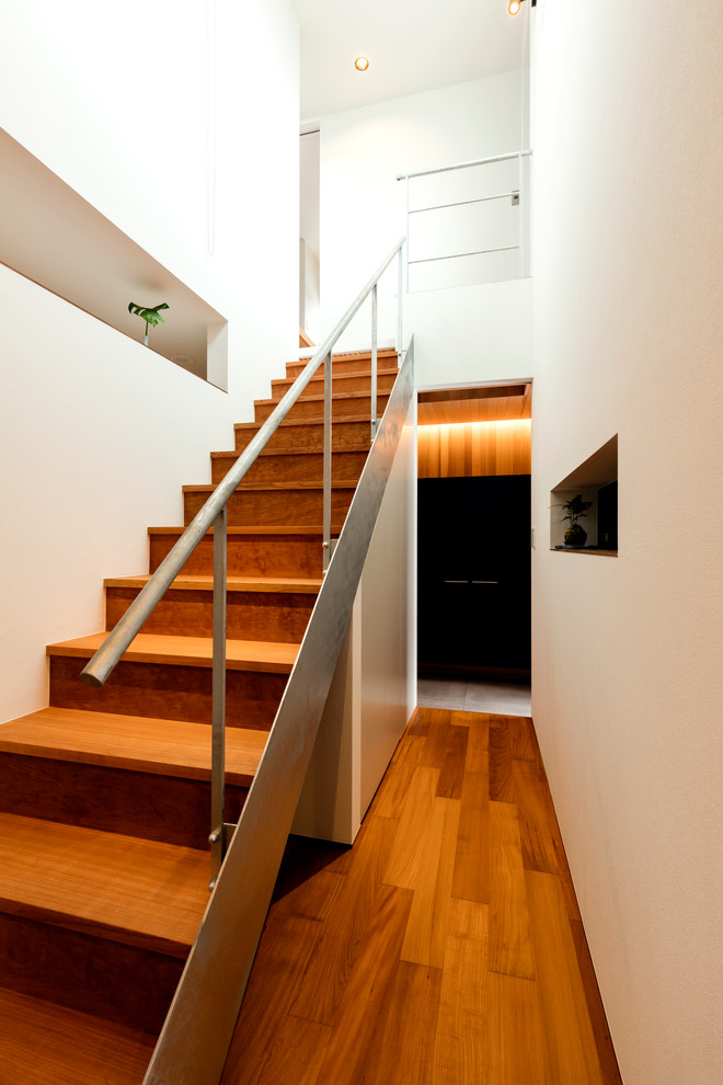 Cette image montre un escalier minimaliste de taille moyenne avec des marches en bois, des contremarches en bois et un garde-corps en métal.