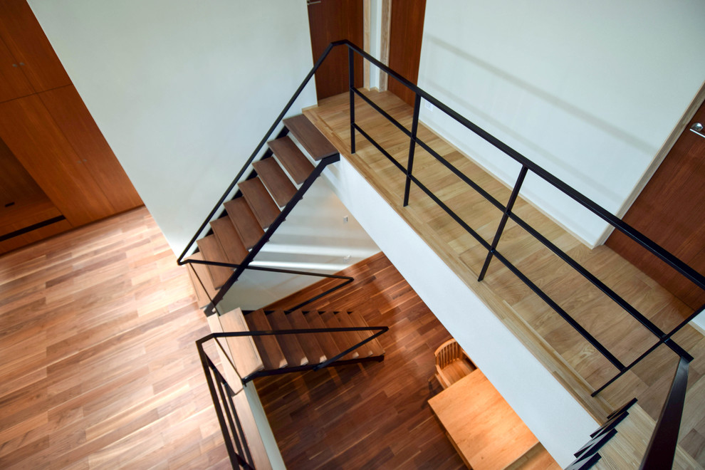 他の地域にある広いコンテンポラリースタイルのおしゃれな折り返し階段 (木の蹴込み板、金属の手すり) の写真