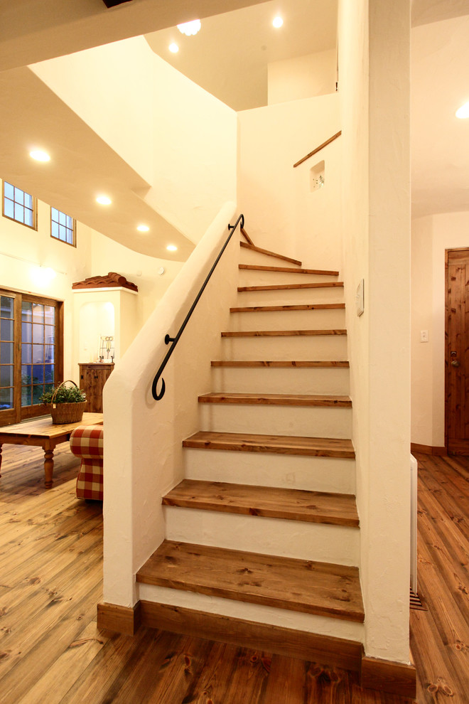 Идея дизайна: изогнутая лестница в стиле кантри с деревянными ступенями и металлическими перилами