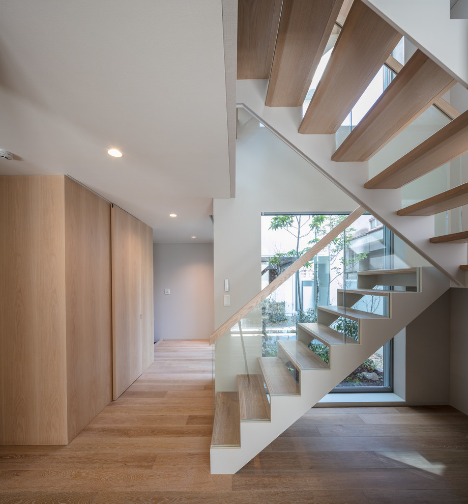 Imagen de escalera en U minimalista sin contrahuella con escalones de madera y barandilla de vidrio