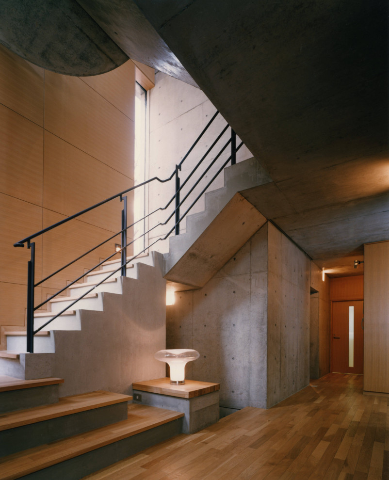 Cette image montre un grand escalier courbe minimaliste avec des marches en bois, des contremarches en béton et un garde-corps en matériaux mixtes.